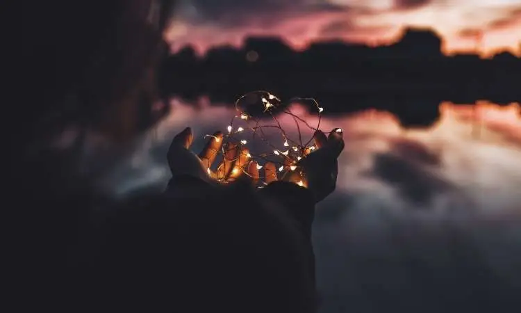 mani tengono dei piccoli fasci di uce al tramonto